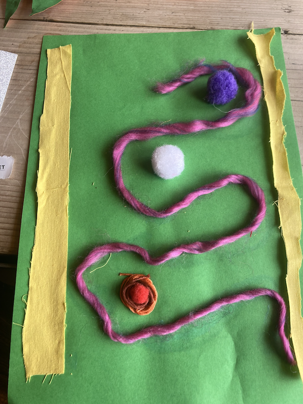 A green paper with a colorful string and balls on it

Description automatically generated with medium confidence